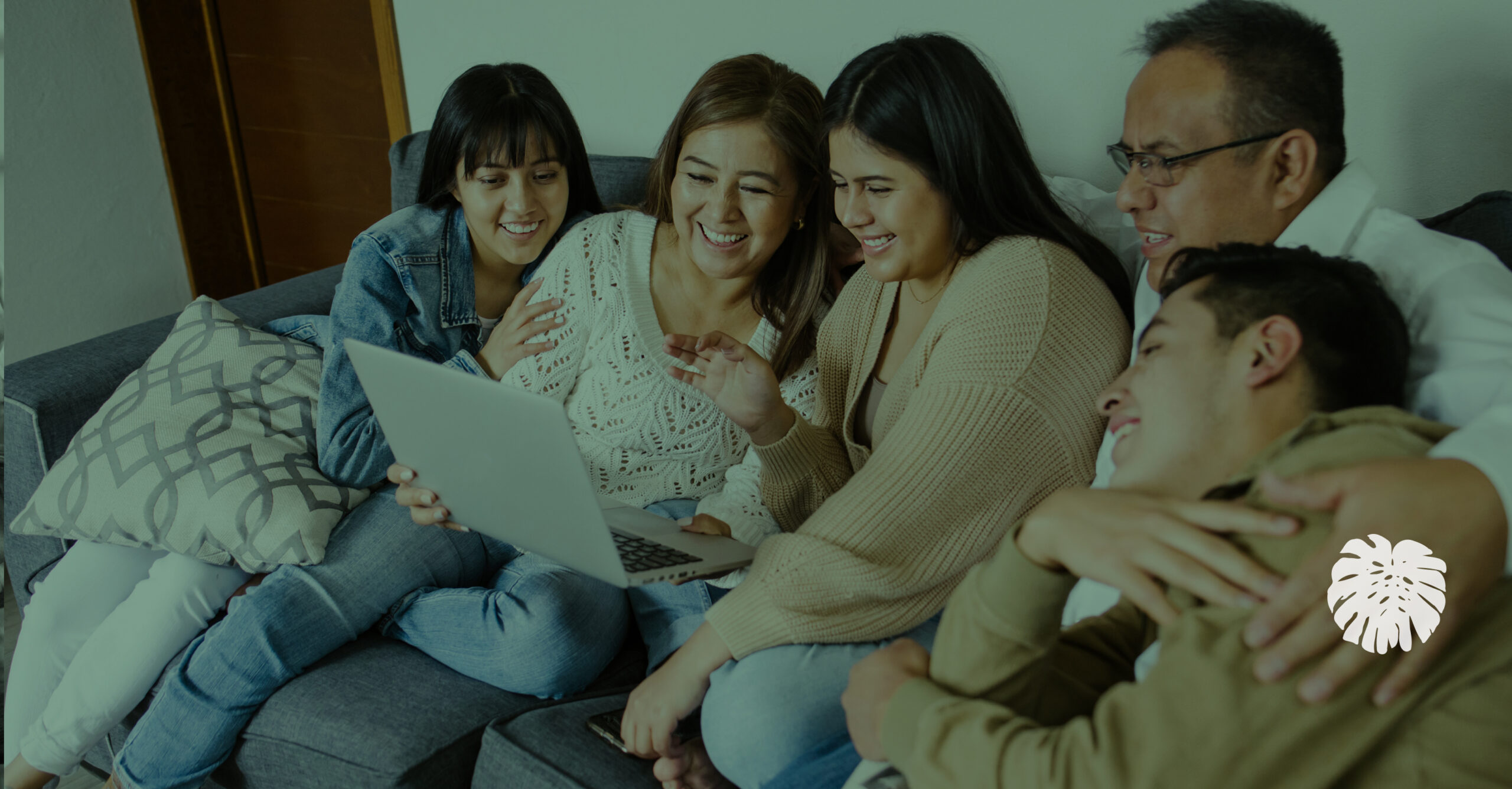 Hispanic family sitting together at home, looking at a laptop and engaging with digital content.